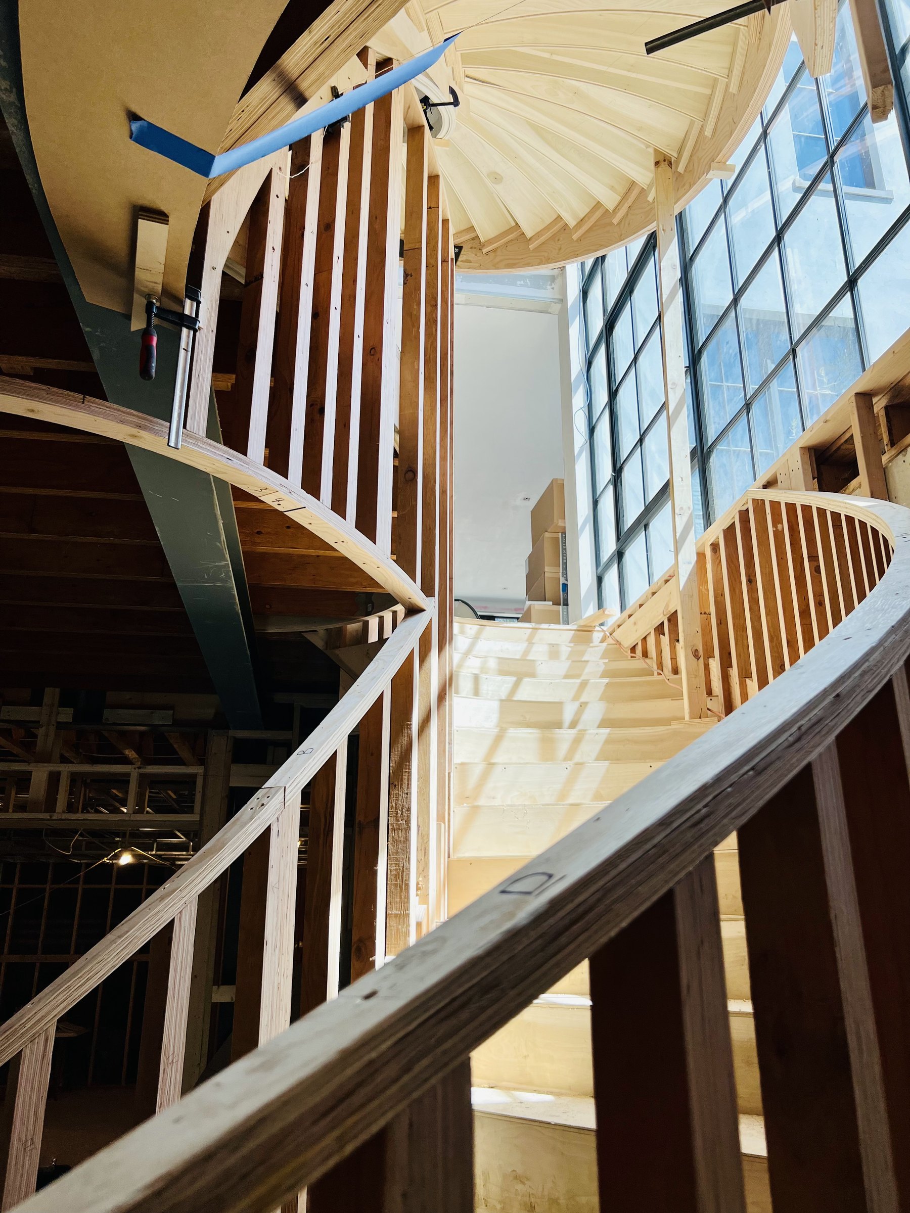 Curved stair being framed in wood beside tall steel windows